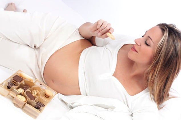Pregnant woman in bed eating chocolate smiling