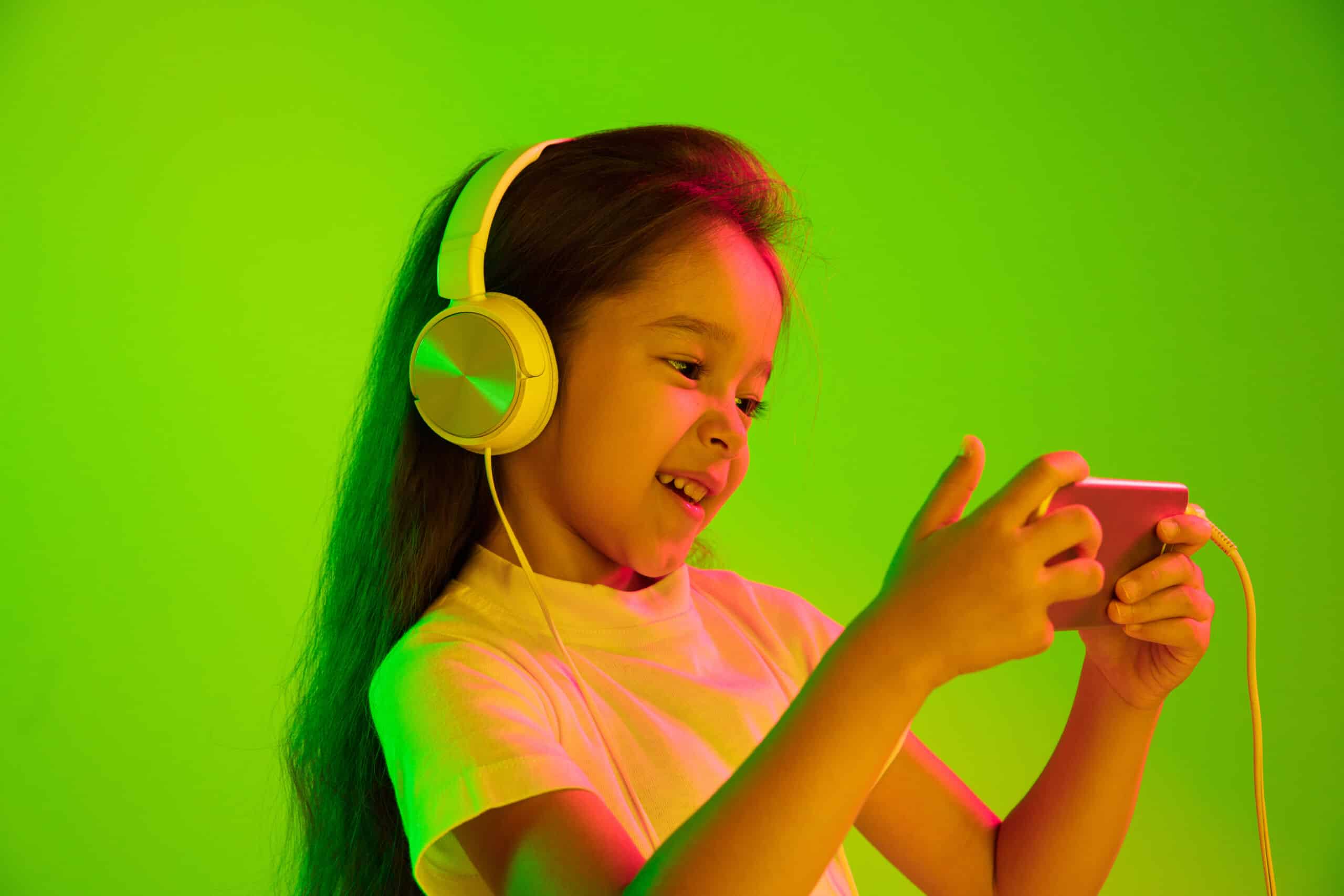 beautiful female half length portrait isolated on green wall in neon light young emotional girl human emotions facial expression concept using smartphone for vlog selfie chating gaming scaled